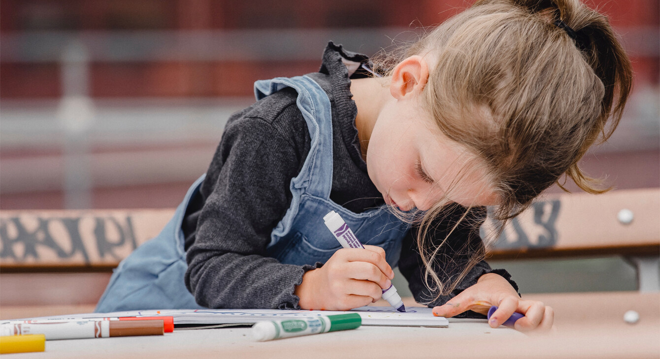 Une petite fille concentrée dessine avec des feutres
