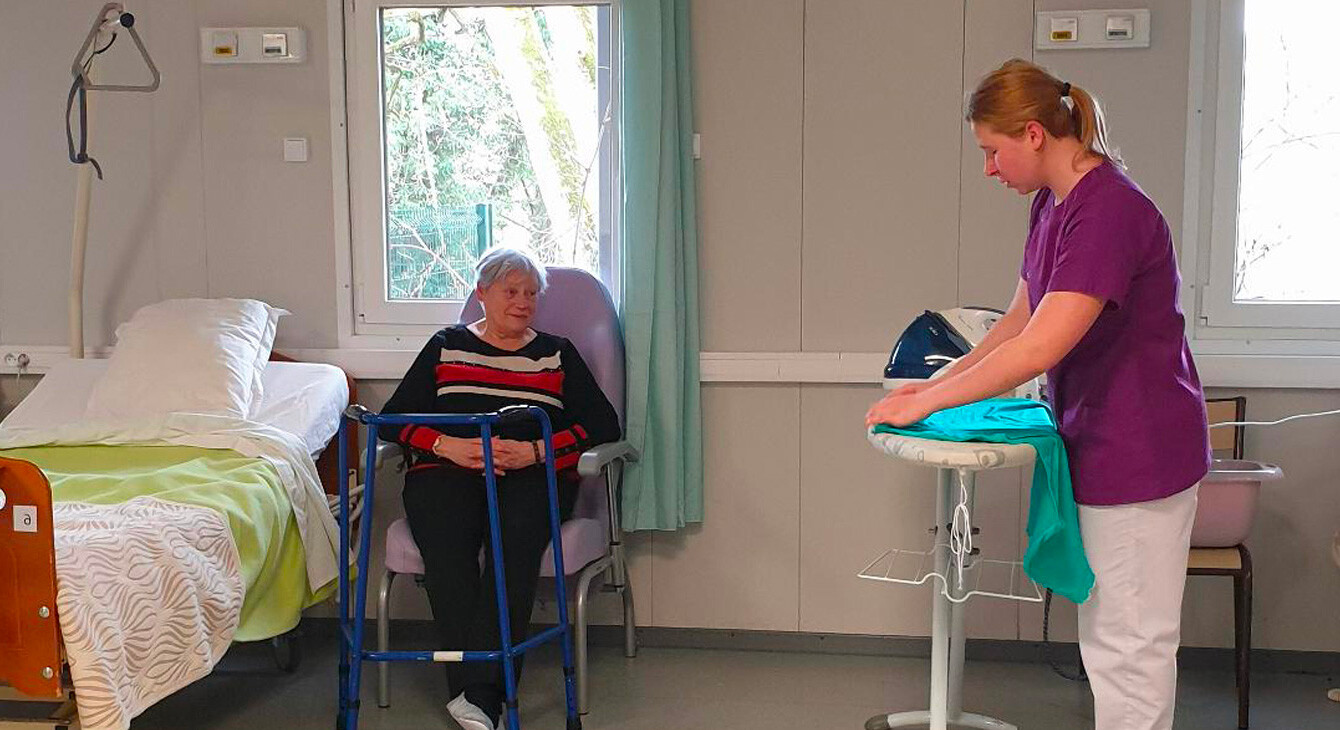 Une jeune fille fait preuve de professionnalisme et de bienveillance lors de la prise en charge de Claudine Thouraine qui joue le rôle d'une personne âgée avec une perte d'autonomie