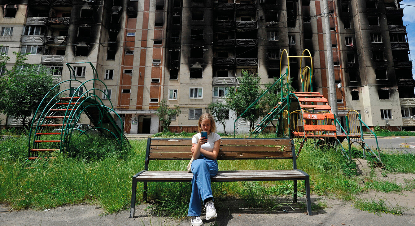 Une jeune fille regarde son smartphone alors qu'elle est assise sur un banc devant des immeubles résidentiels partiellement détruits à la suite du bombardement de la ville d'Irpin, près de la capitale ukrainienne Kyiv le 16 juin 2022, alors que la guerre russo-ukrainienne entre dans son 113ème jour