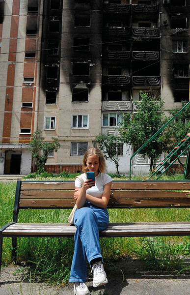 Une jeune fille regarde son smartphone alors qu'elle est assise sur un banc devant des immeubles résidentiels partiellement détruits à la suite du bombardement de la ville d'Irpin, près de la capitale ukrainienne Kyiv le 16 juin 2022, alors que la guerre russo-ukrainienne entre dans son 113ème jour