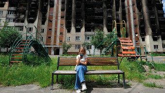 Une jeune fille regarde son smartphone alors qu'elle est assise sur un banc devant des immeubles résidentiels partiellement détruits à la suite du bombardement de la ville d'Irpin, près de la capitale ukrainienne Kyiv le 16 juin 2022, alors que la guerre russo-ukrainienne entre dans son 113ème jour
