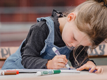 Une petite fille concentrée dessine avec des feutres