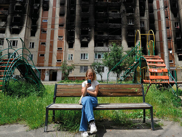 Une jeune fille regarde son smartphone alors qu'elle est assise sur un banc devant des immeubles résidentiels partiellement détruits à la suite du bombardement de la ville d'Irpin, près de la capitale ukrainienne Kyiv le 16 juin 2022, alors que la guerre russo-ukrainienne entre dans son 113ème jour